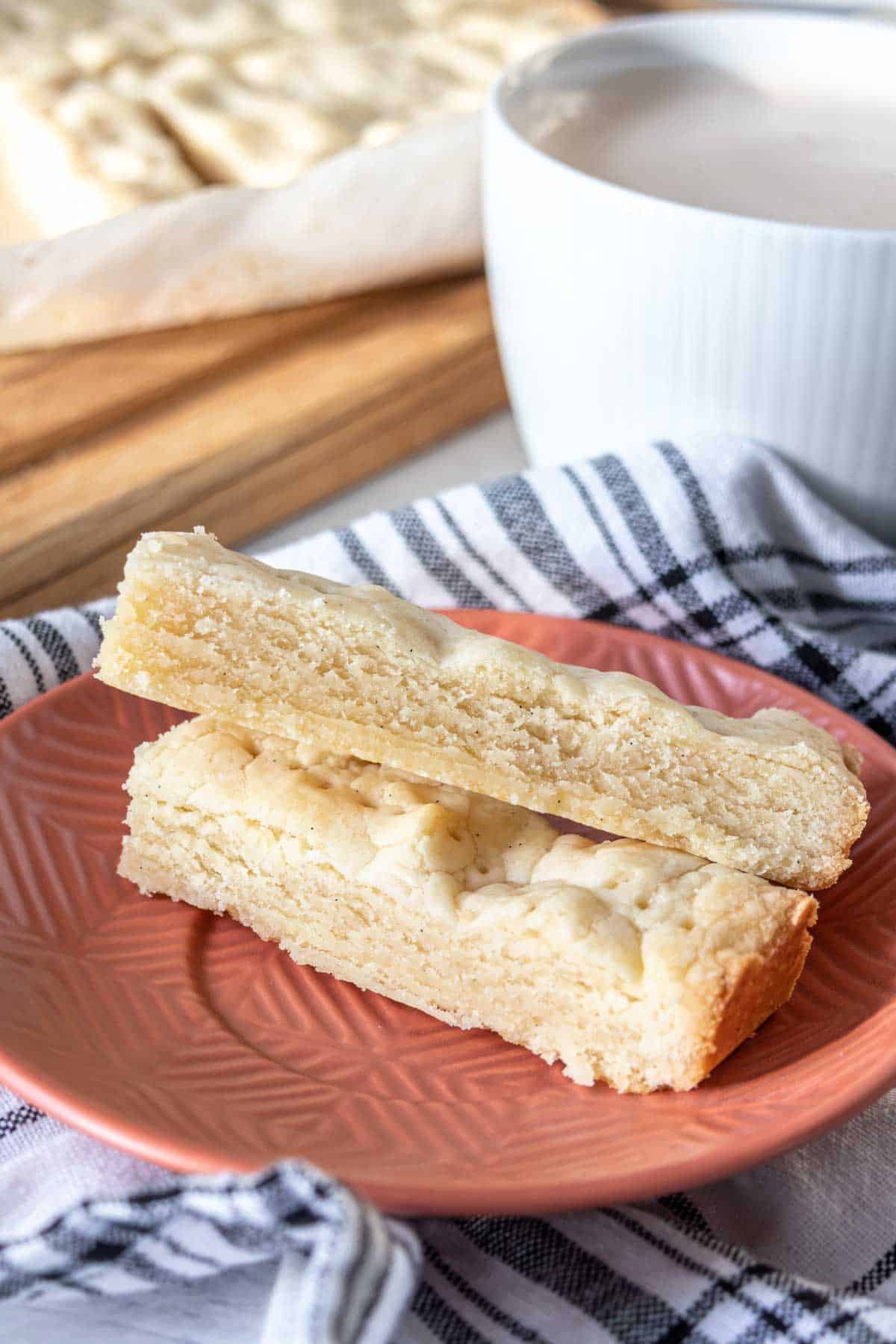 Two pieces of shortbread stacked on an orange plate showing the cookie texture.