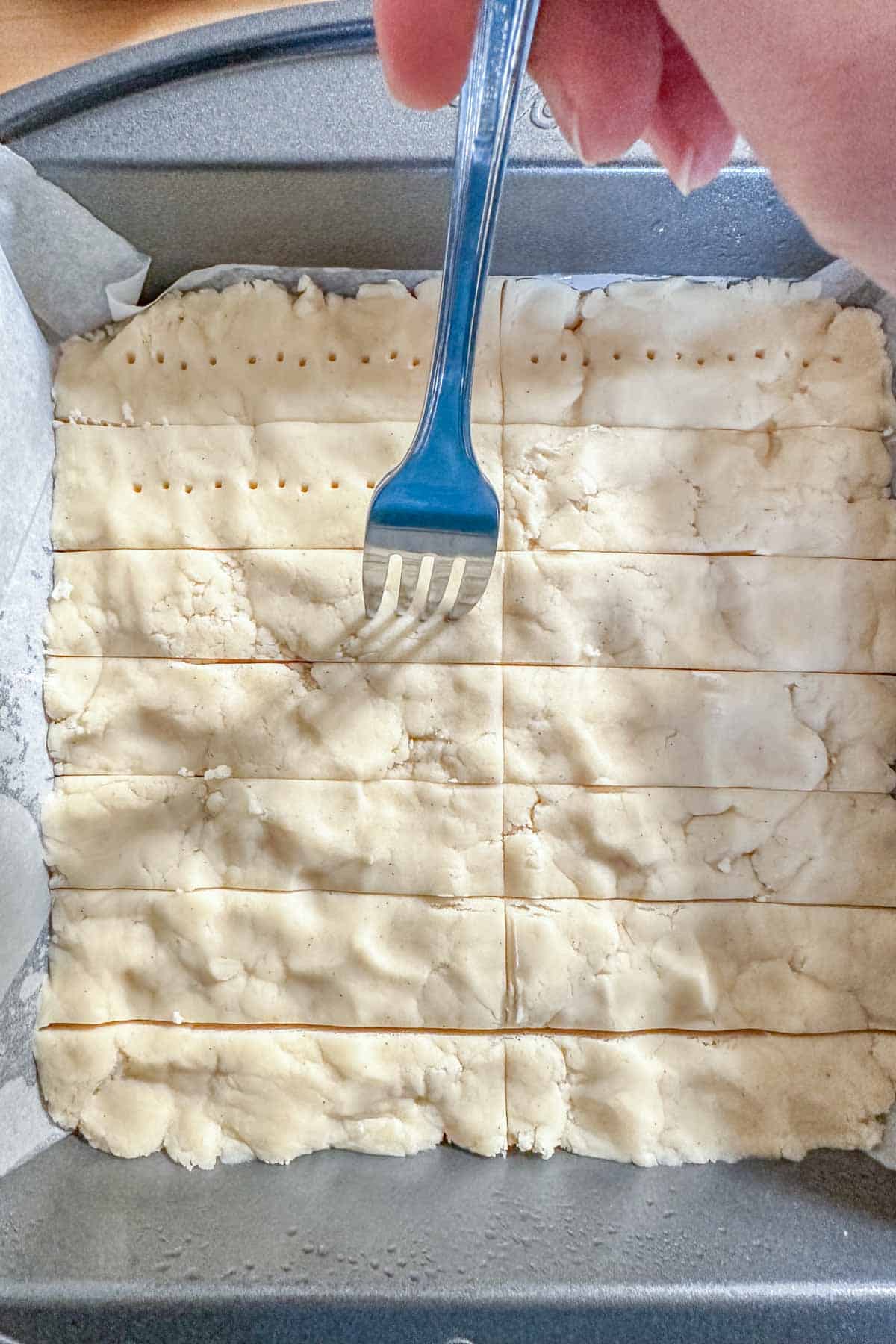 Using a fork to dock shortbread cookie dough.