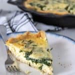 Slice of spinach quiche on a plate with a fork.