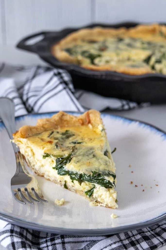 Slice of spinach quiche on a plate with a fork.