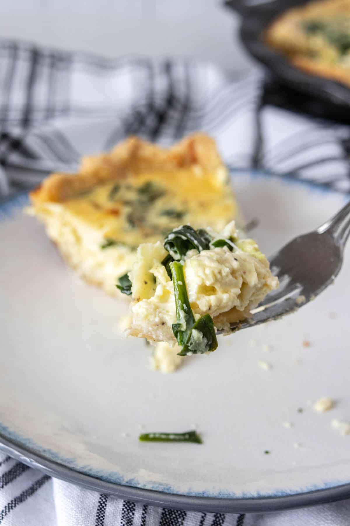 Fork holding up bite of spinach quiche.