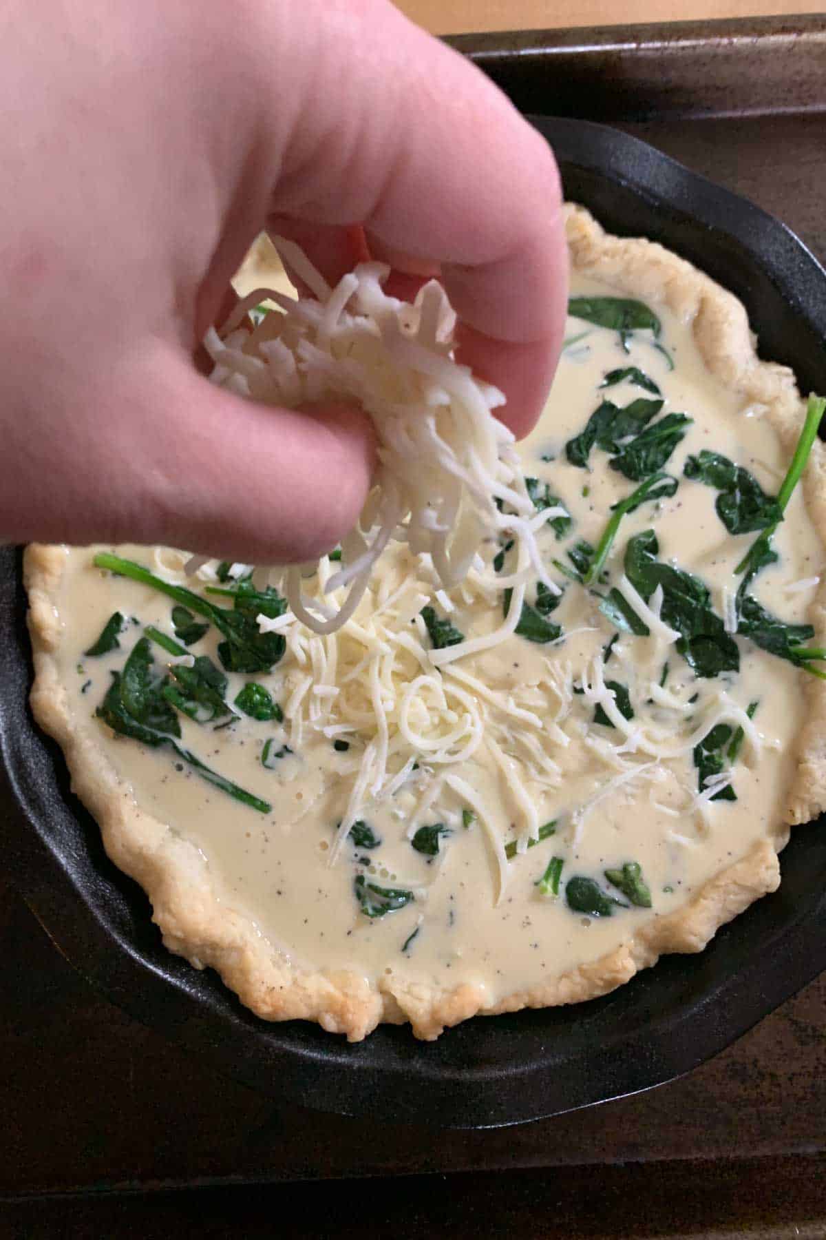 Adding cheese on top of unbaked spinach quiche.