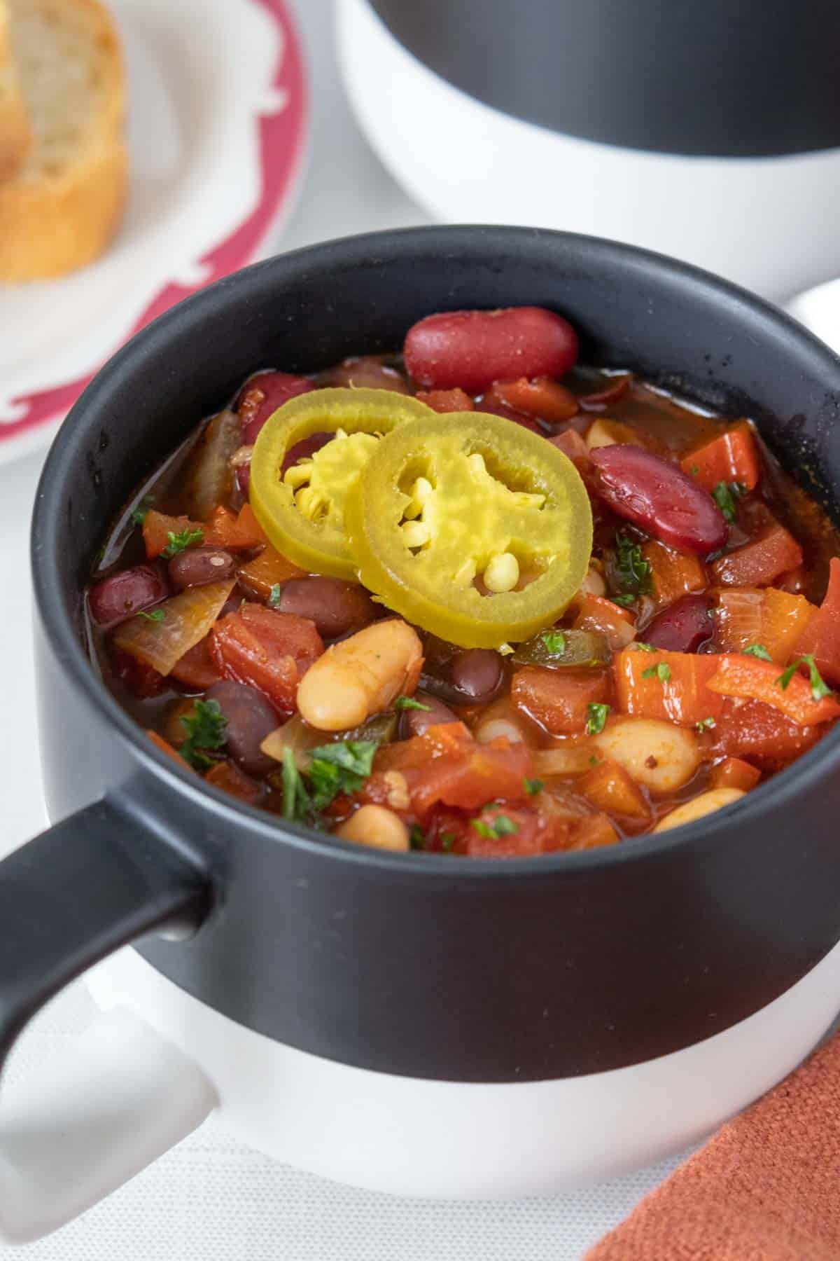 Black and white mug of three bean chili with pickled jalapeno slices.