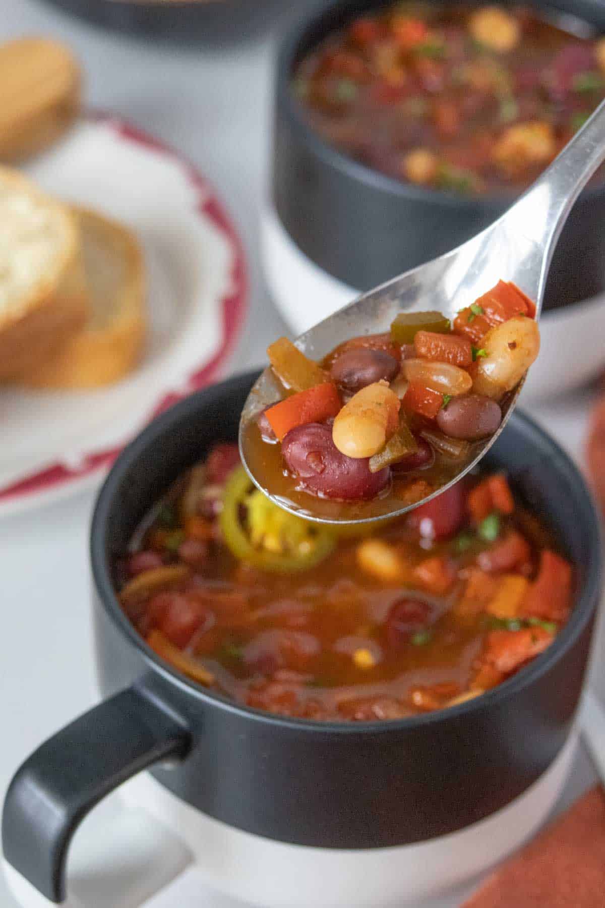 Spoonful of three bean chili held above a black and white colorblocked mug full of chili.