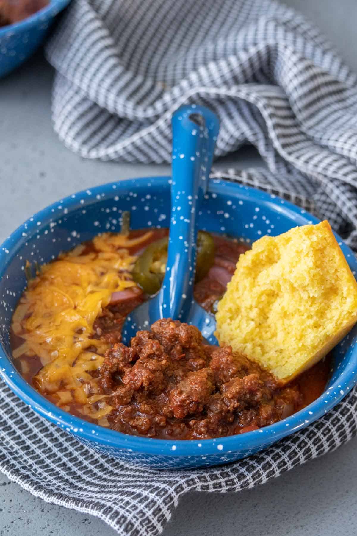 Bison chili in a blue bowl with a corn muffin half on top.