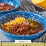 Blue bowls filled with hearty bison chili, topped with shredded cheese, jalapeños, and onions; cornbread on a plate in the background.