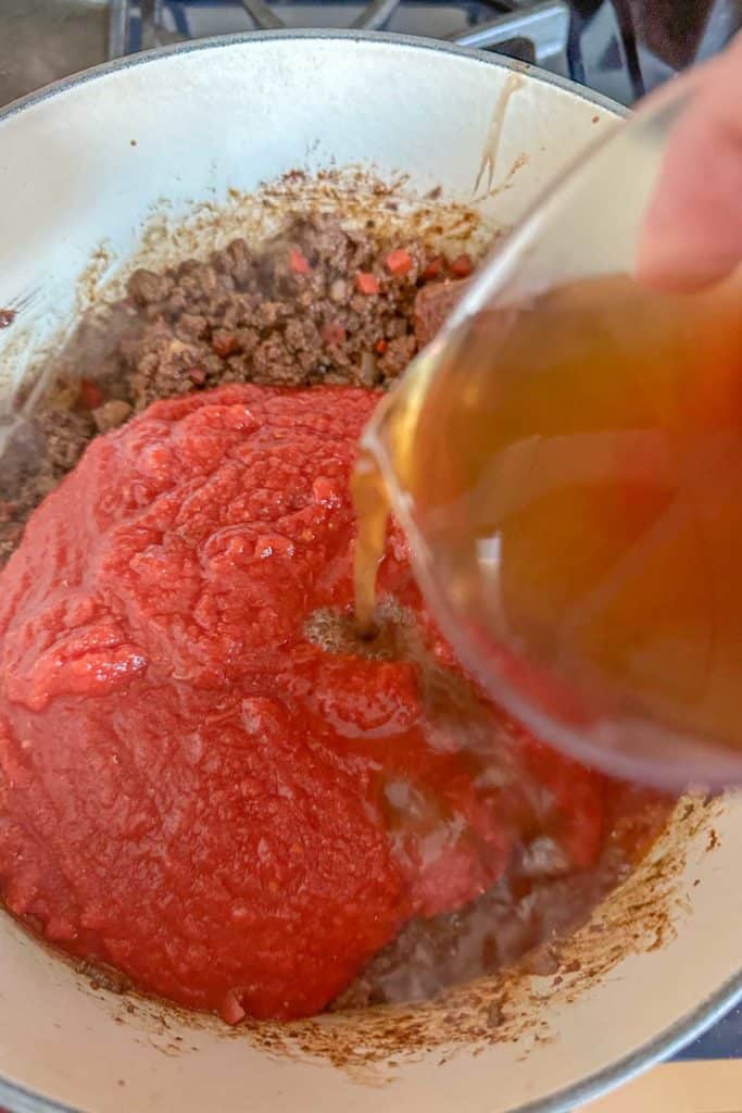 Adding tomatoes and broth to bison chili.