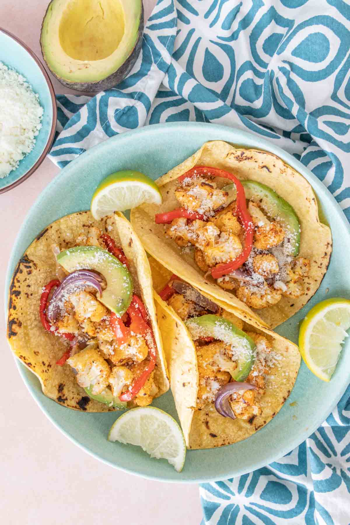 Overhead of three cauliflower tacos on a blue plate with a blue patterned napkin.