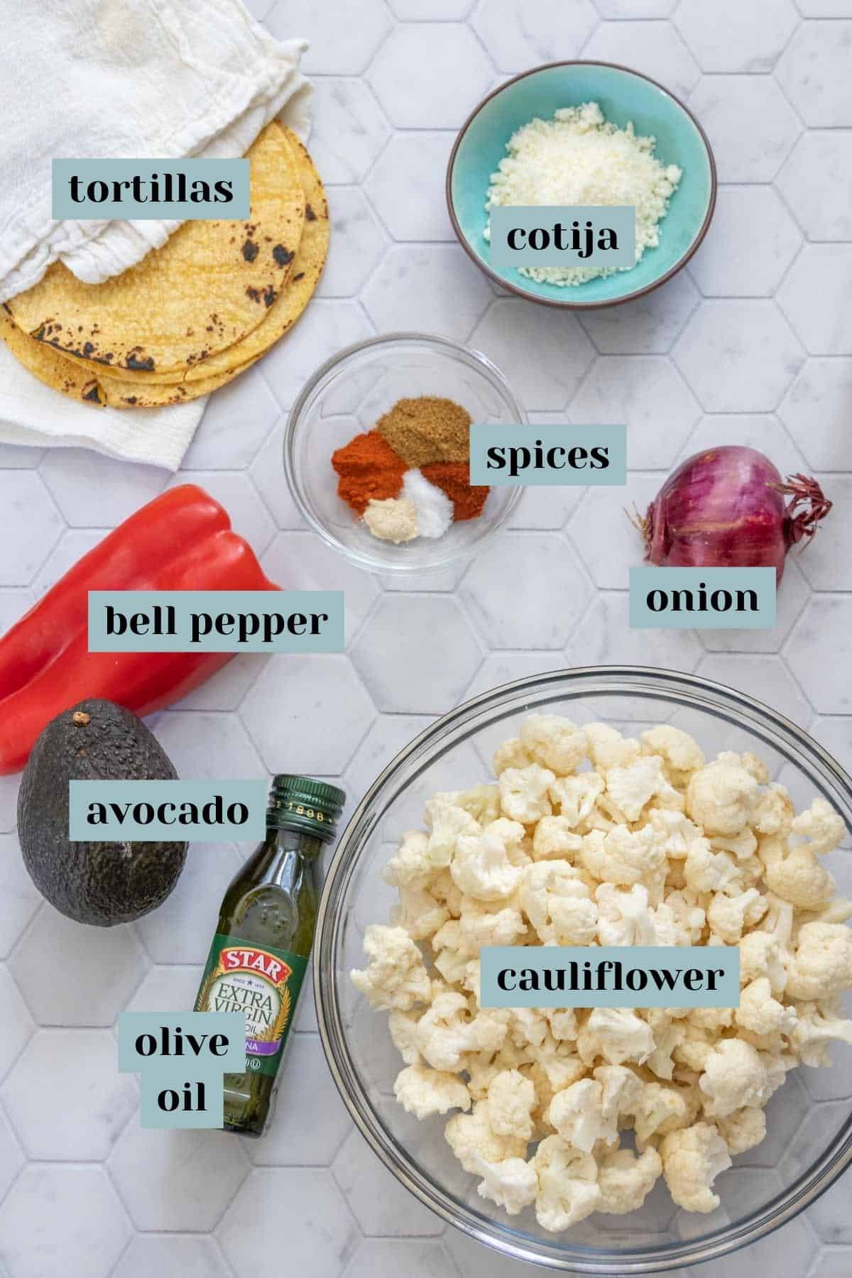 Ingredients for cauliflower tacos on tile surface with labels.