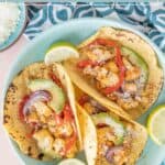 Three roasted cauliflower tacos with red bell pepper, onions, avocado slices, and cheese on corn tortillas, garnished with lime wedges on a blue plate—perfect for anyone craving flavorful cauliflower tacos.