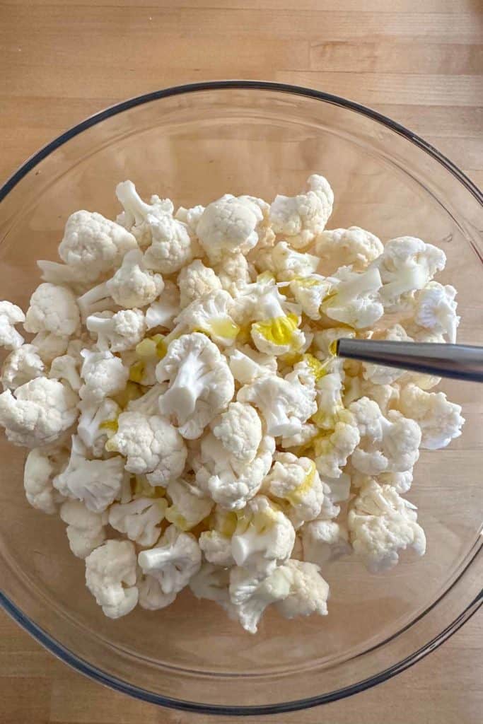 Pouring olive oil onto cauliflower in a glass bowl.