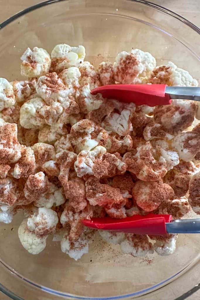 Mixing spices onto cauliflower in a glass bowl.