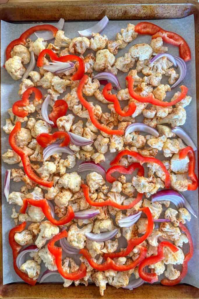 Cauliflower, red bell pepper, and red onion on a baking sheet.