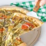 Slice of chicken pesto pizza being held up on a server.