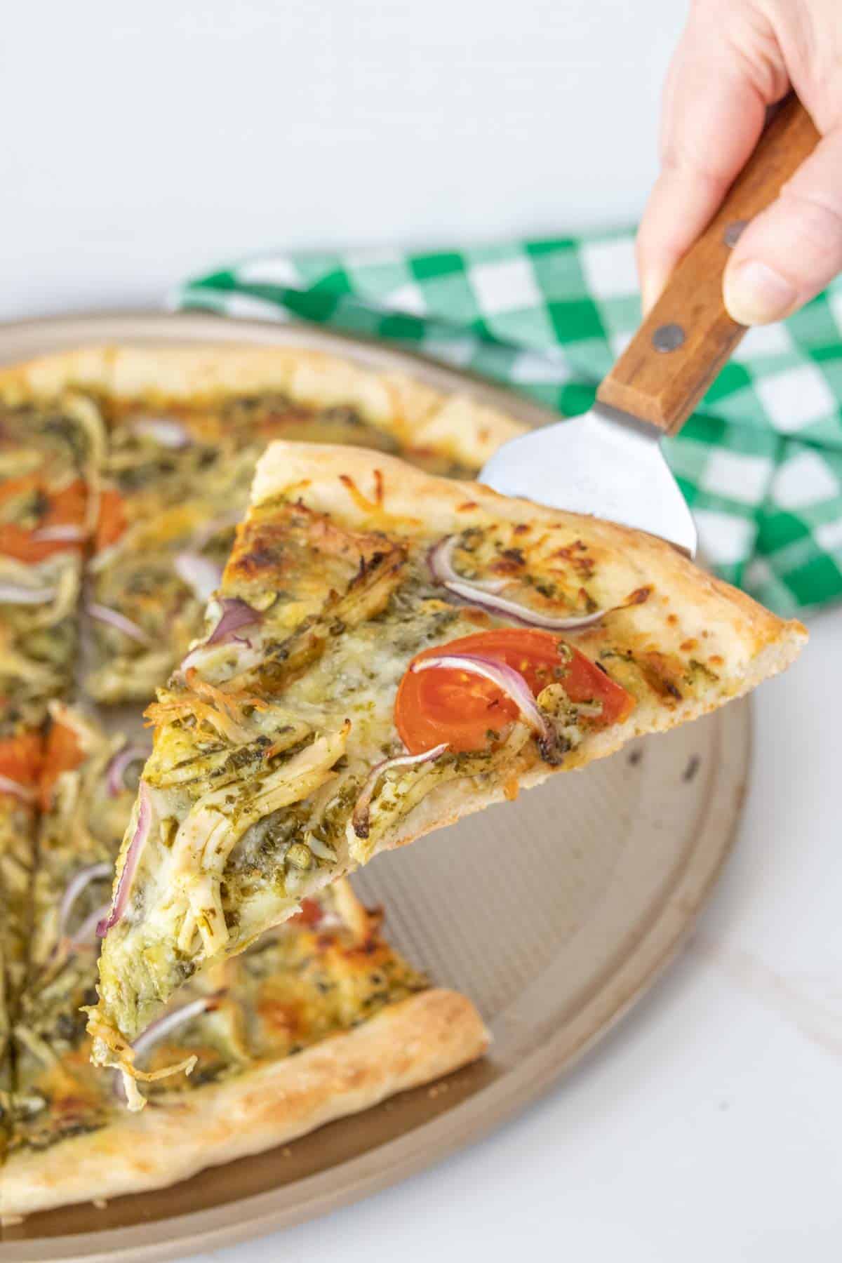 Slice of chicken pesto pizza being held up on a server.