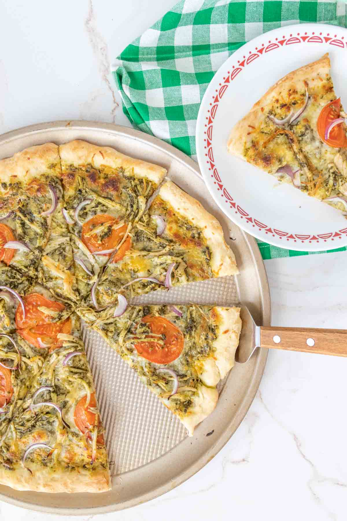 Chicken pesto pizza on a pizza pan sliced and being served.