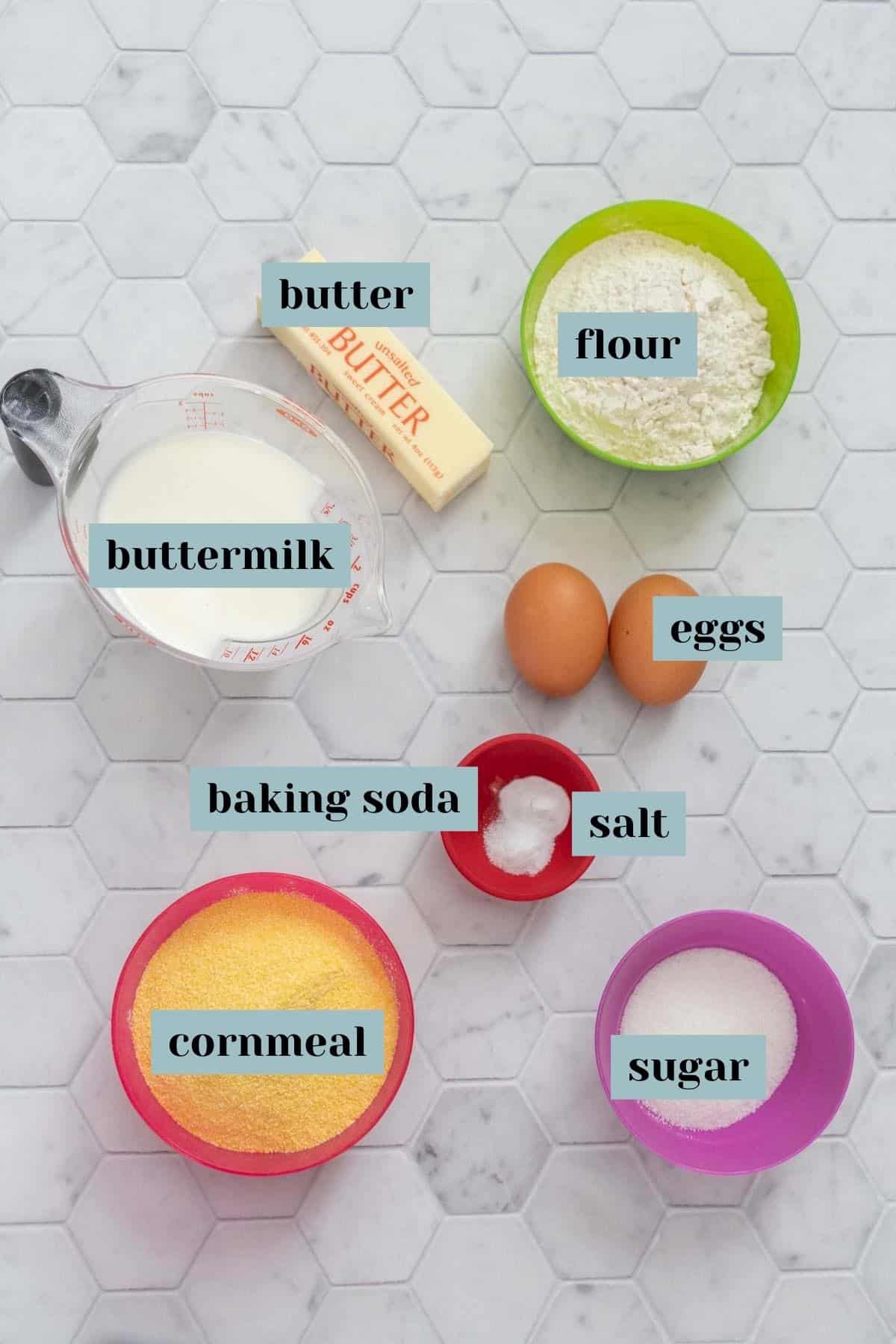 Ingredients for corn muffins and corn bread on a tile surface with labels.