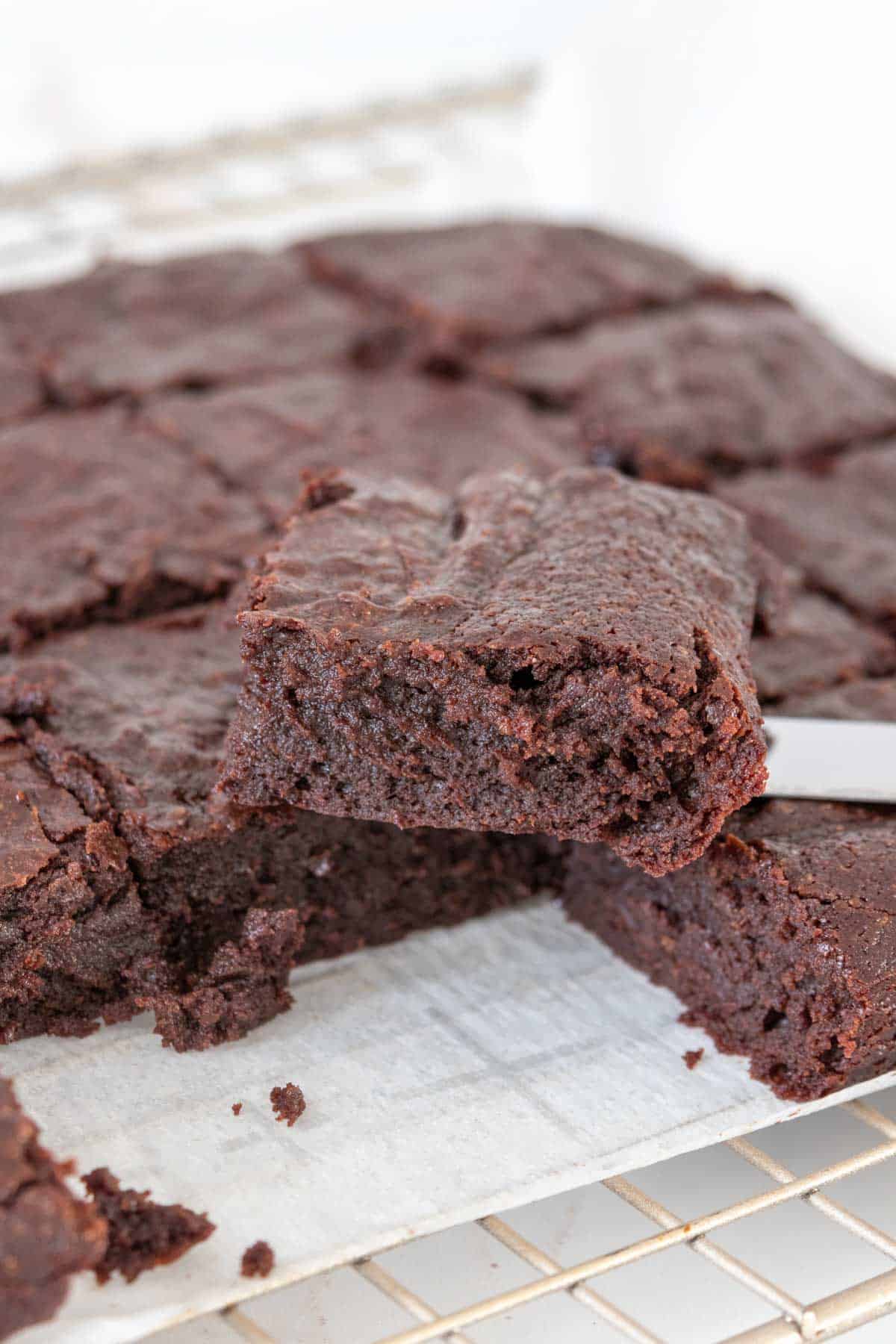 Sliced fudgy brownies on a cooling rack with one stacked on top.