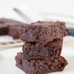 Three stacked fudgy brownies on a white plate.