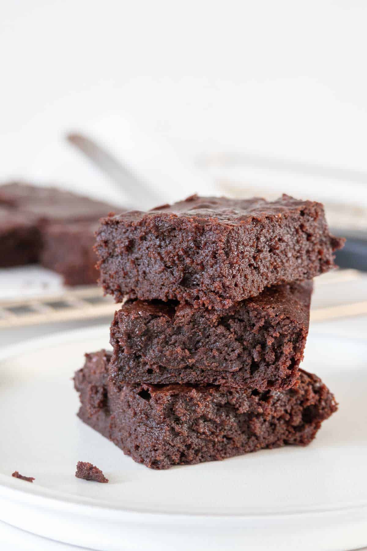 Three stacked fudgy brownies on a white plate.