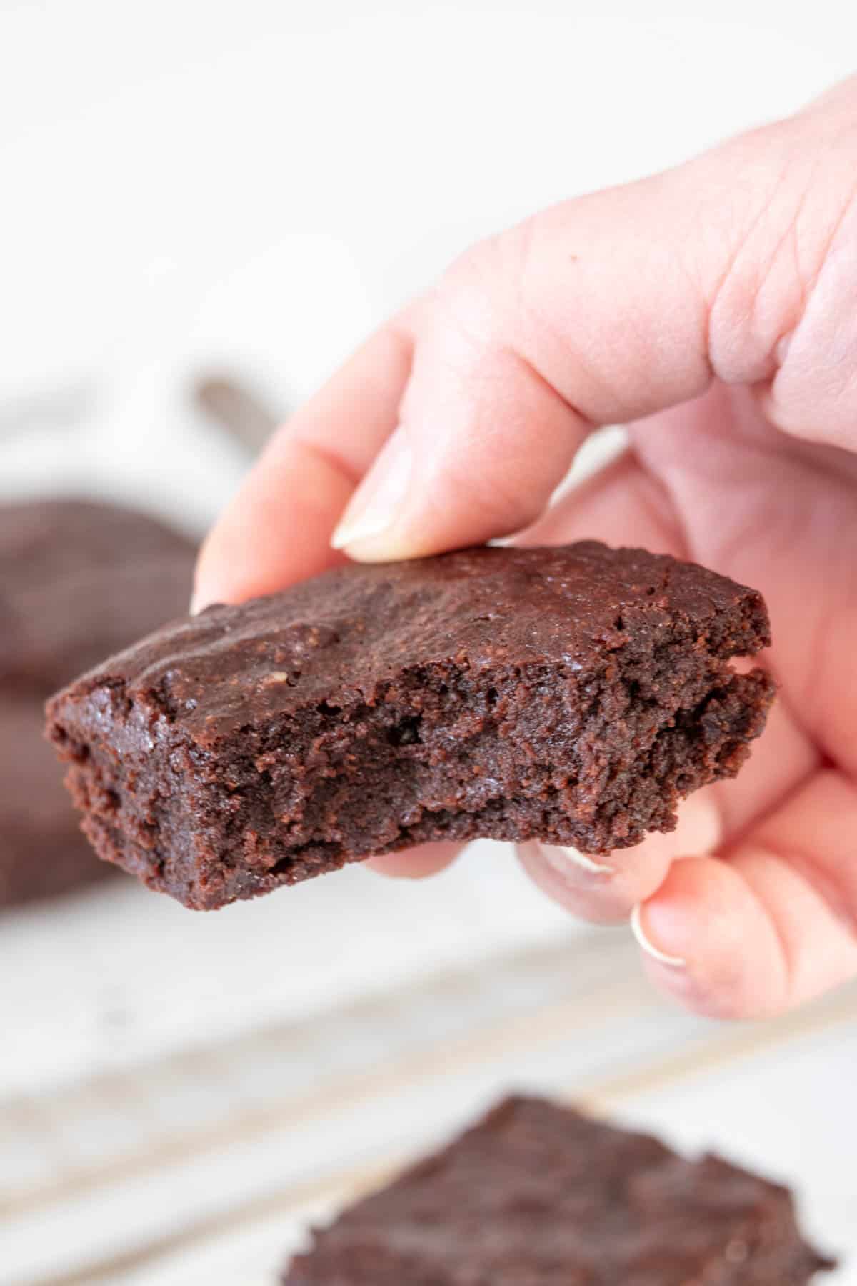 Caucasian hand holding a fudgy brownie with a bite taken.