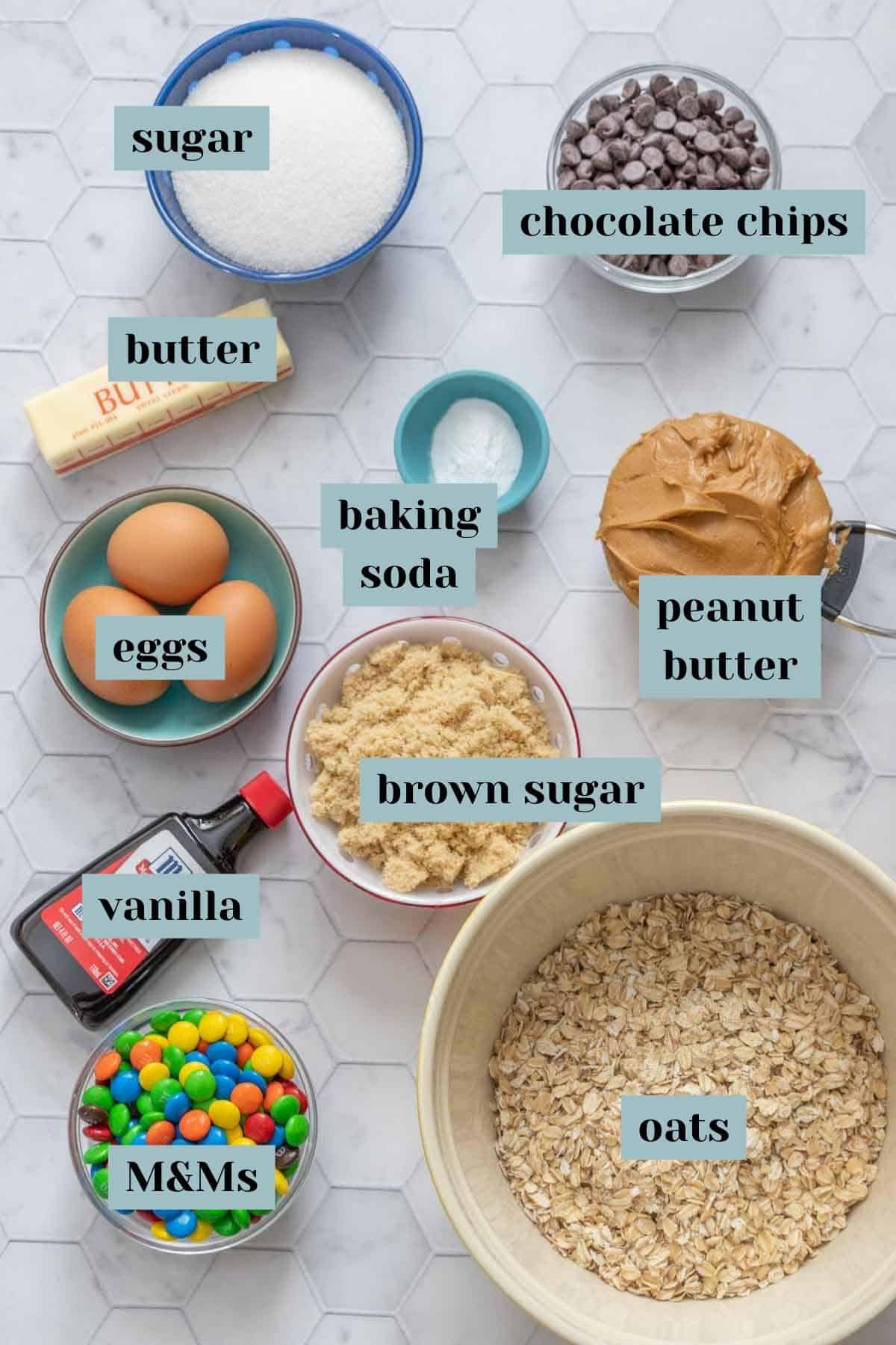 Ingredients for monster cookies on a tile surface with labels.