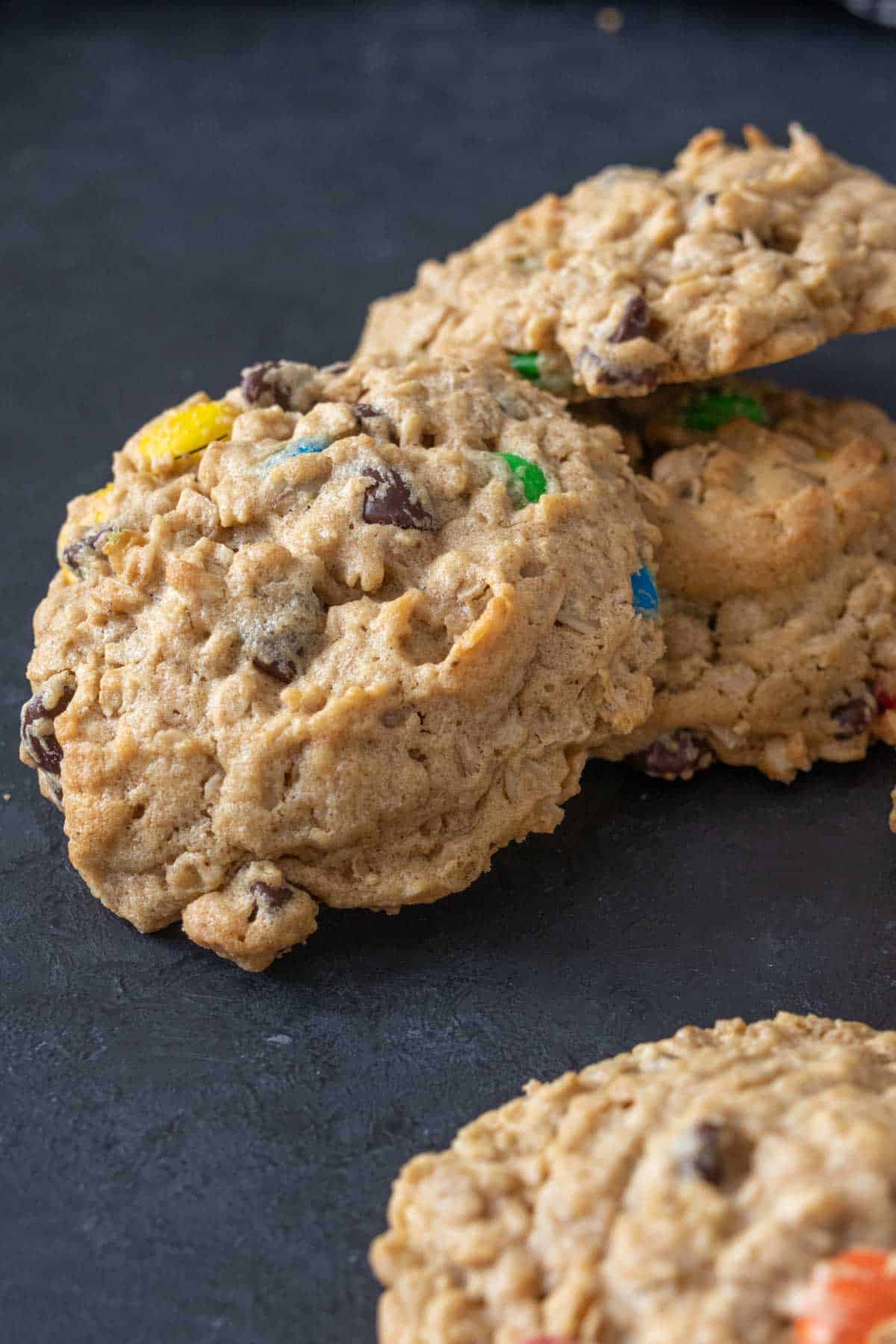 Pile of monster cookies on a dark countertop.