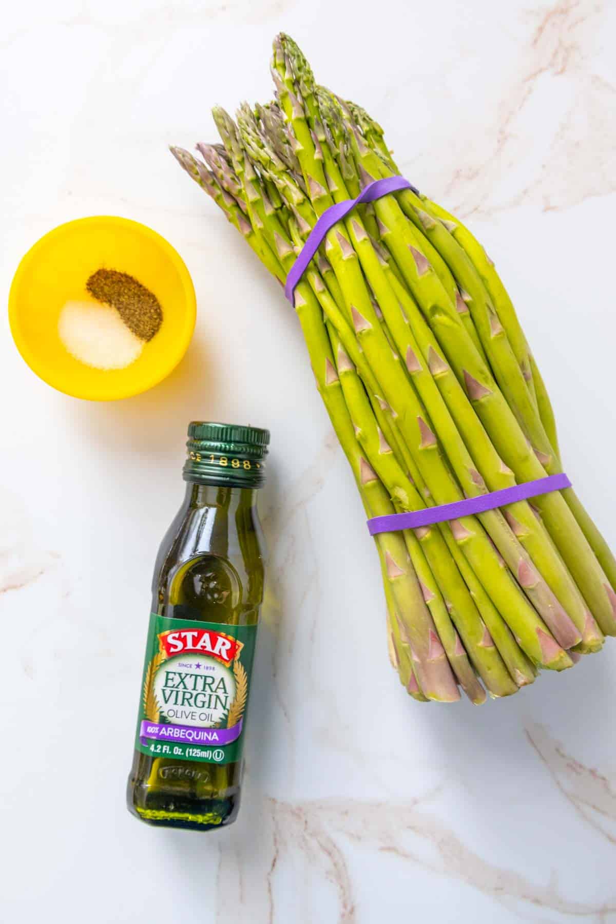 Ingredients for roasted asparagus on a marble surface.