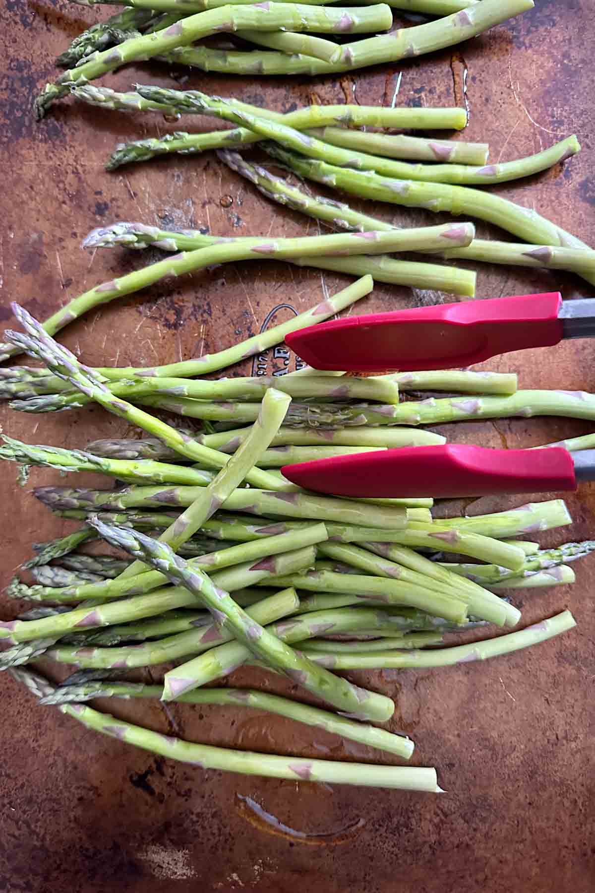 Tossing asparagus on baking sheet to coat with olive oil.