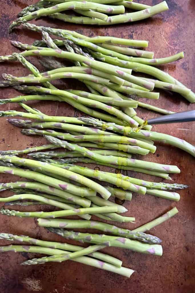 Drizzling olive oil onto asparagus spears.