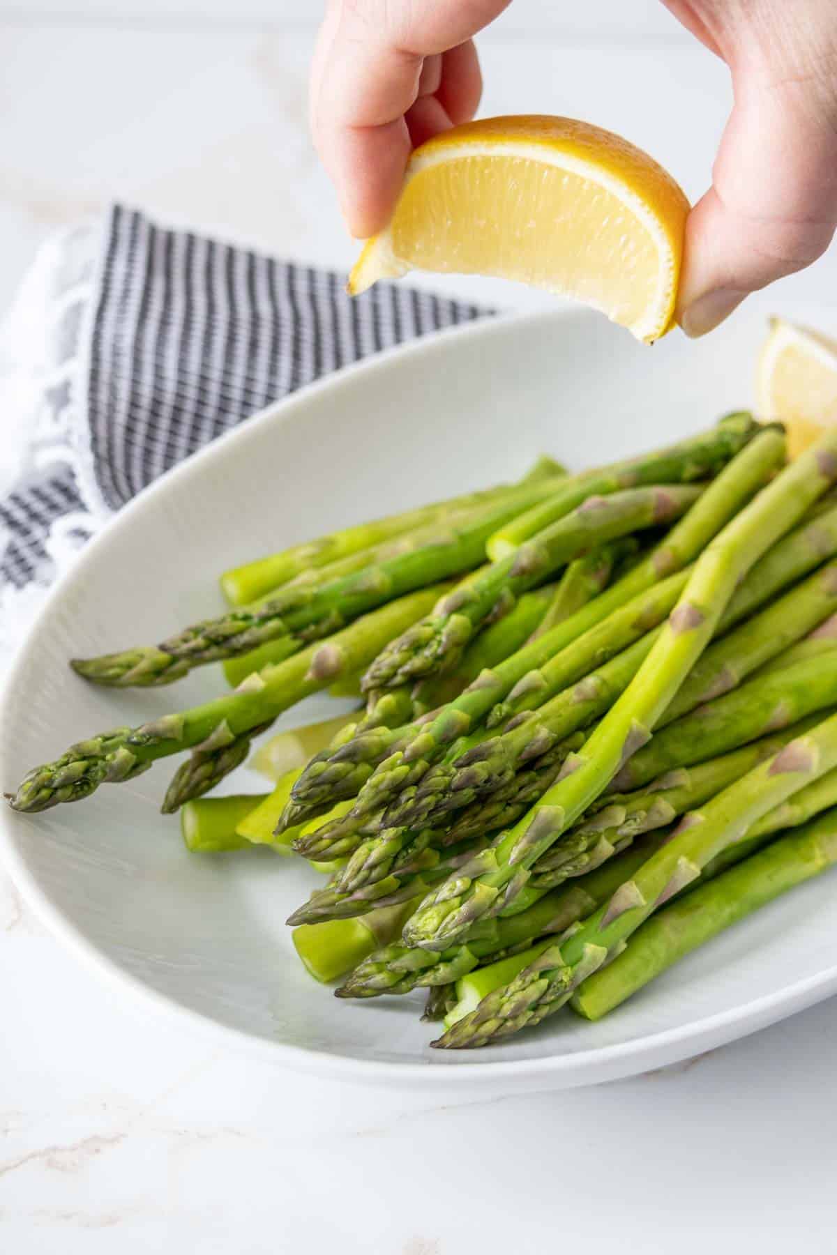 Caucasian hand squeezing lemon onto a platter of steamed asparagus.