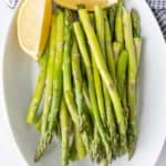 Steamed asparagus spears on a white platter with lemon quarters.