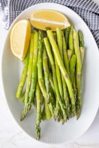Steamed asparagus spears on a white platter with lemon quarters.
