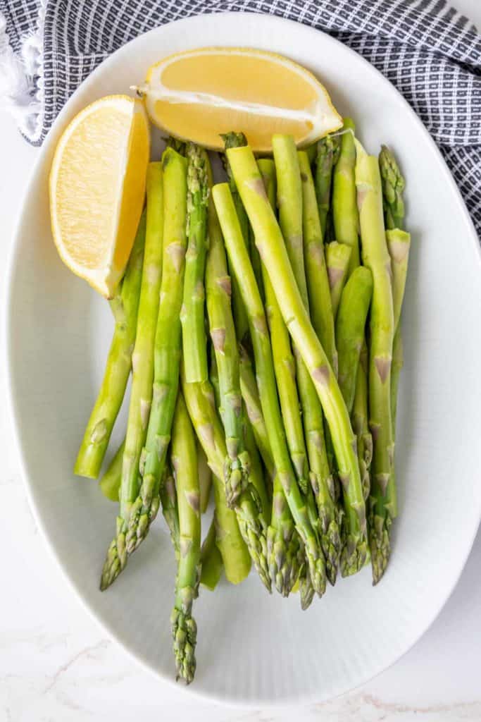 Steamed asparagus spears on a white platter with lemon quarters.