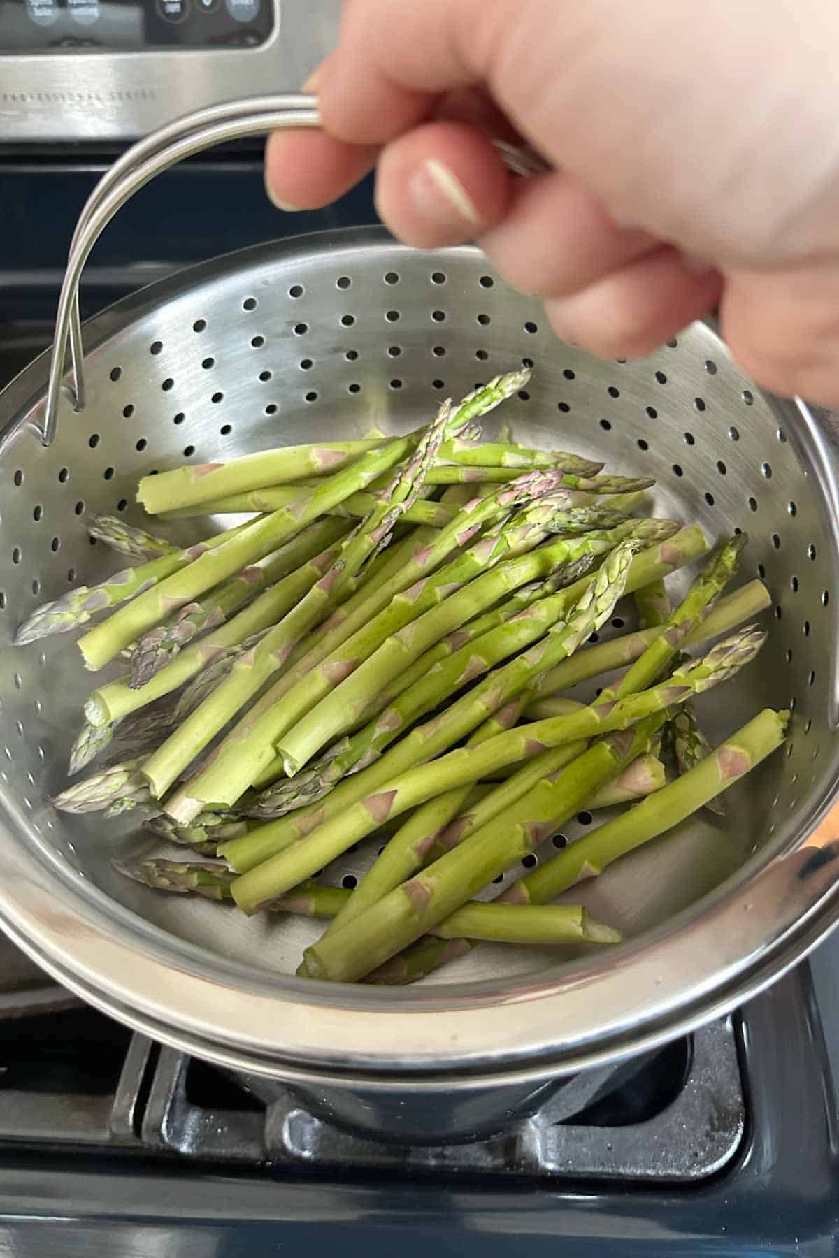 Placing a steamer basket full of asparagus on a steamer pot.