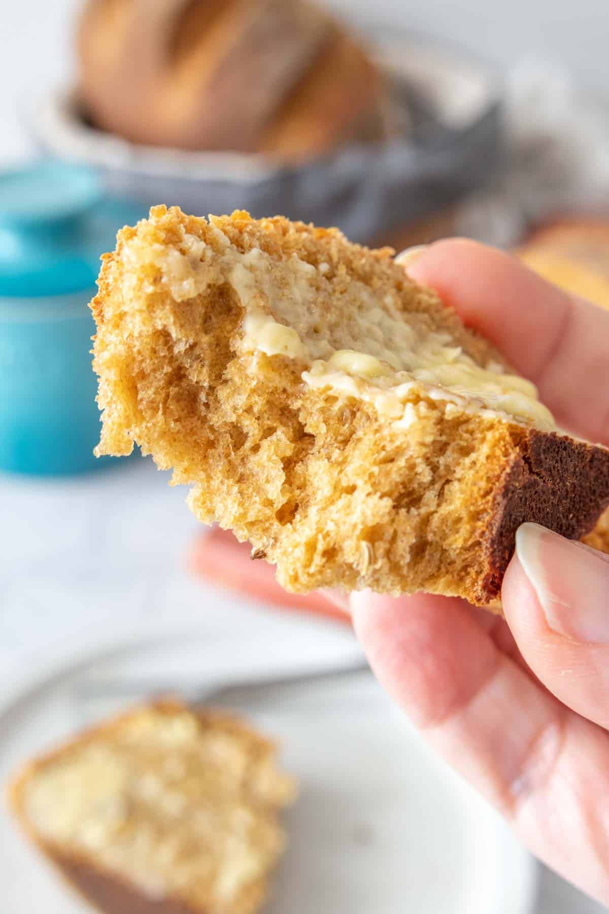 Torn slice of limpa bread with butter on it held close to camera to see interior texture.