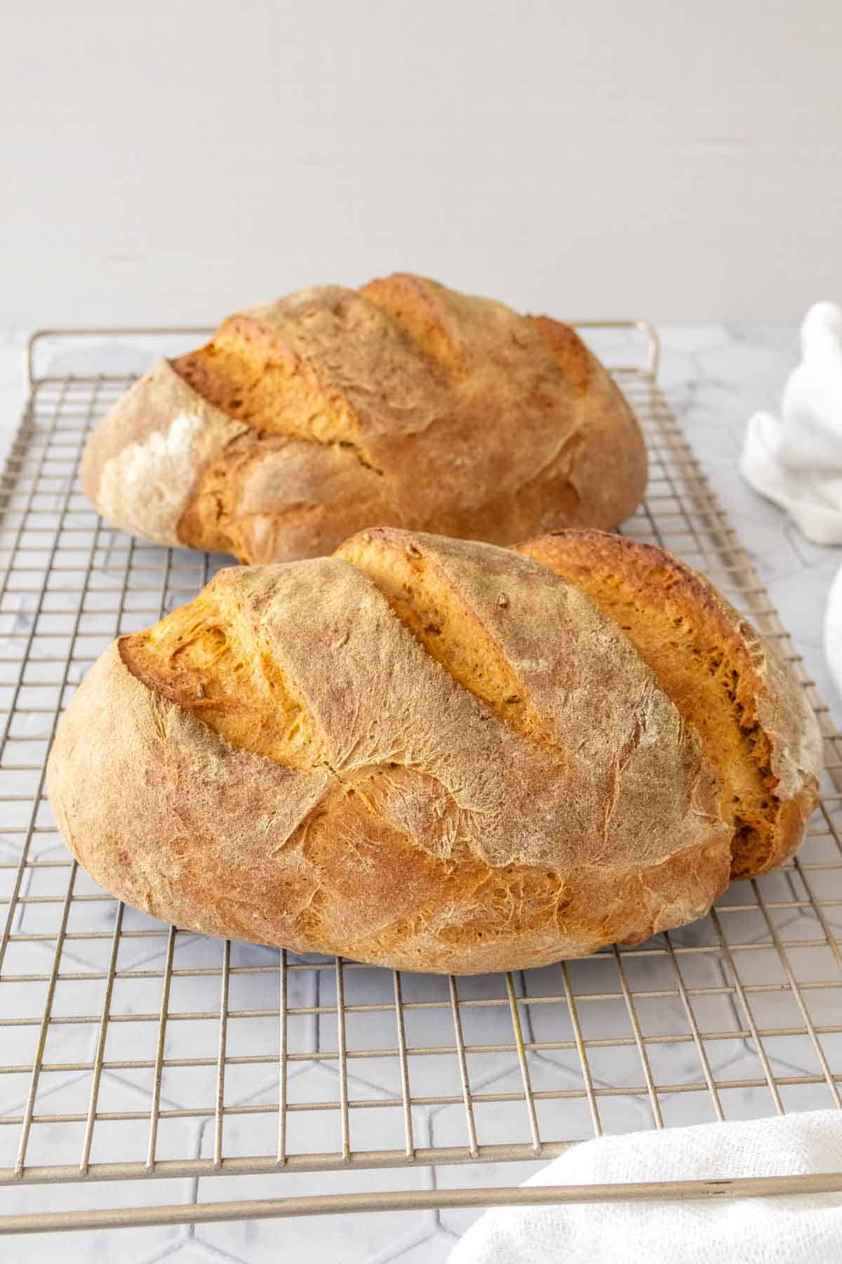 Two loaves of limpa cooling on a wire rack.