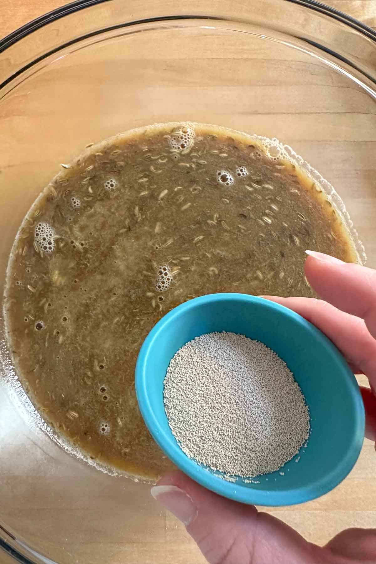 Yeast in a blue pinch bowl over a mixing bowl of warmed liquid ingredients for limpa.