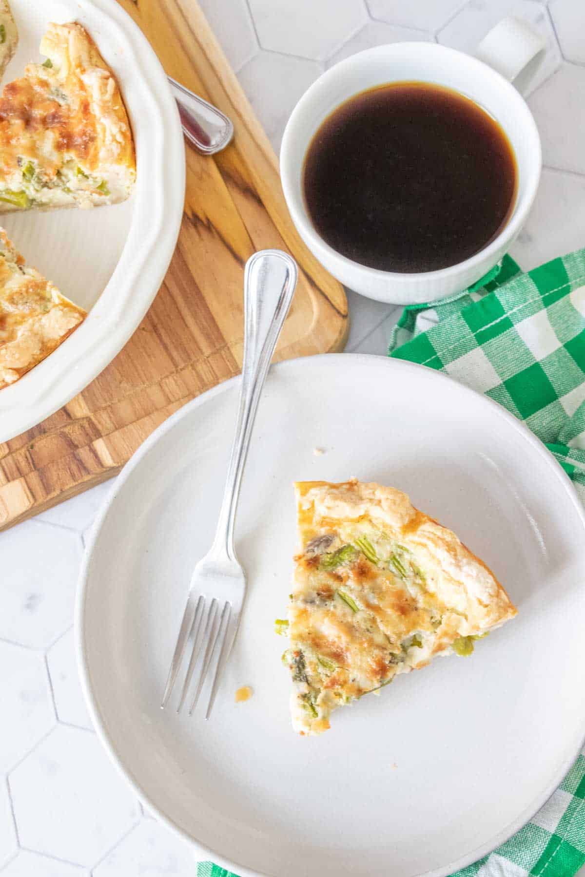 Overhead photo of a slice of asparagus quiche on a gray plate with a cup of coffee beside.