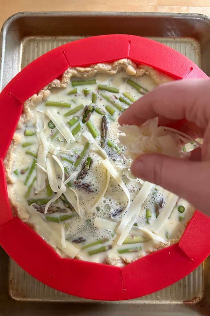 Adding cheese on top of unbaked asparagus quiche.