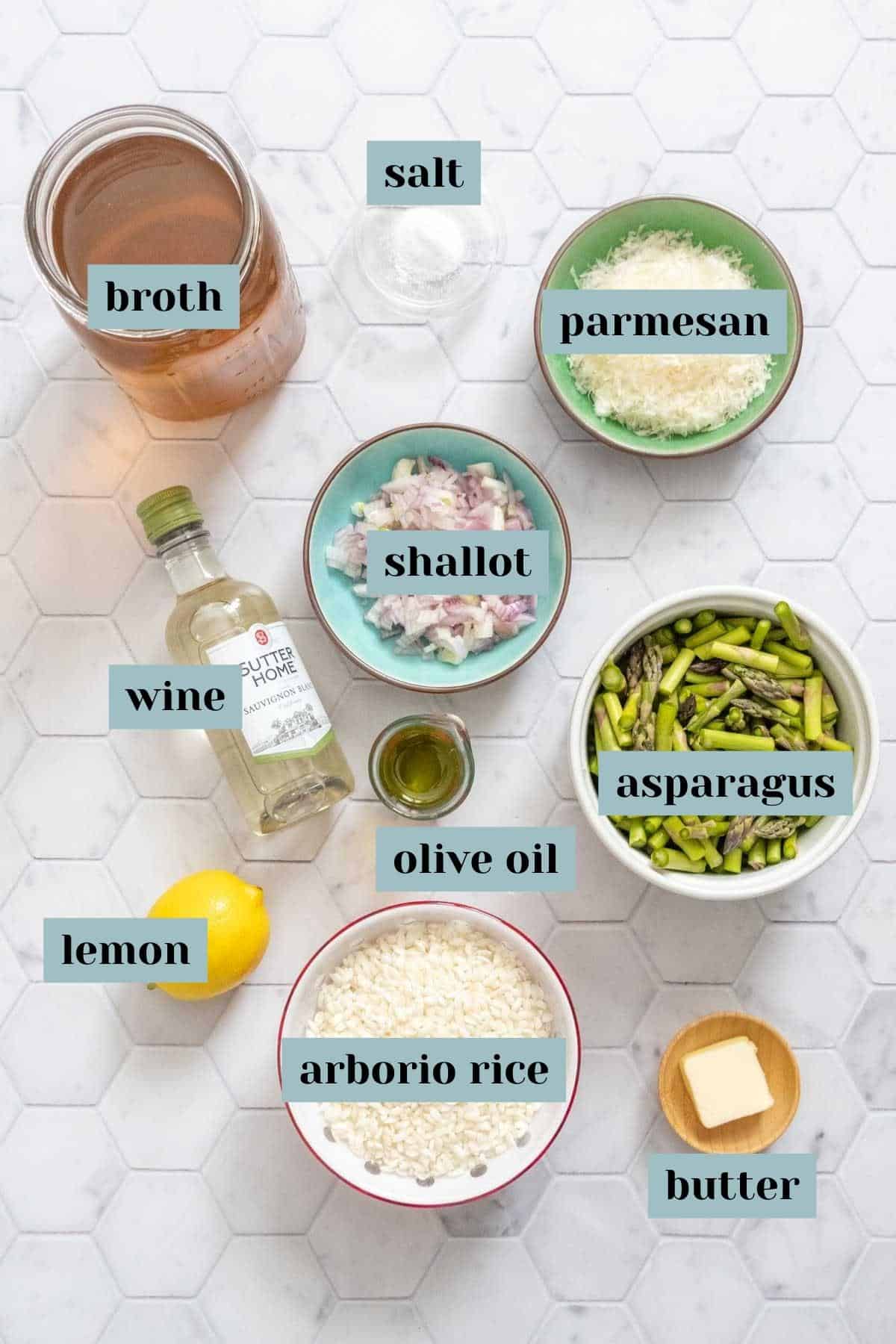 Ingredients for asparagus risotto on a tile surface with labels.