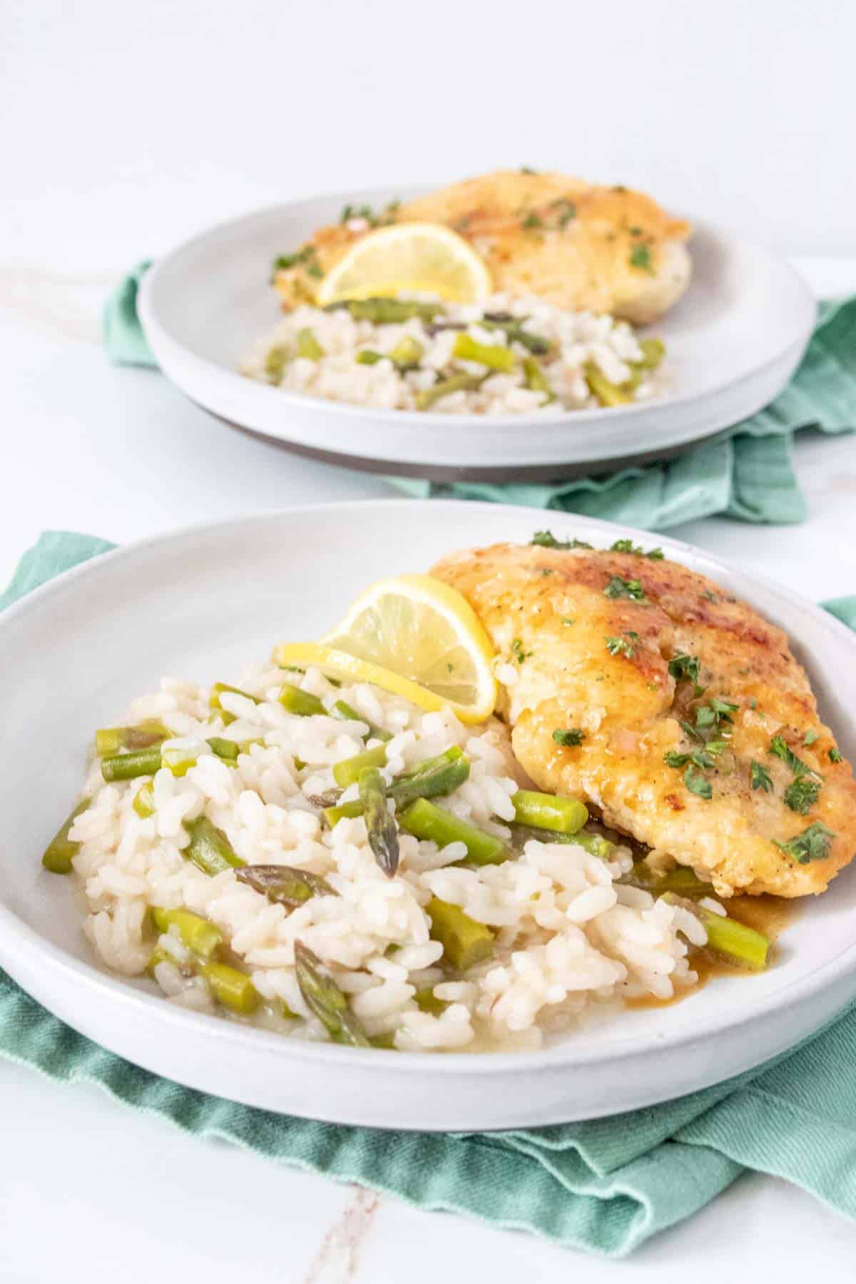 Two plates of asparagus risotto and chicken with lemon.
