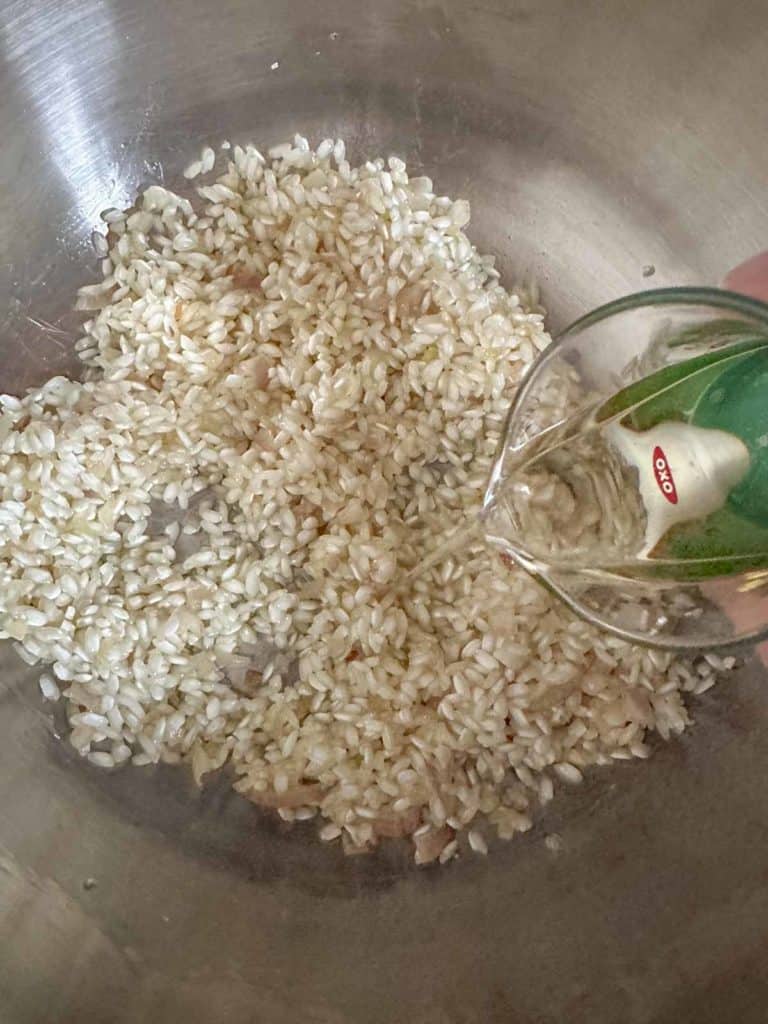 Adding wine to rice in pan for risotto.