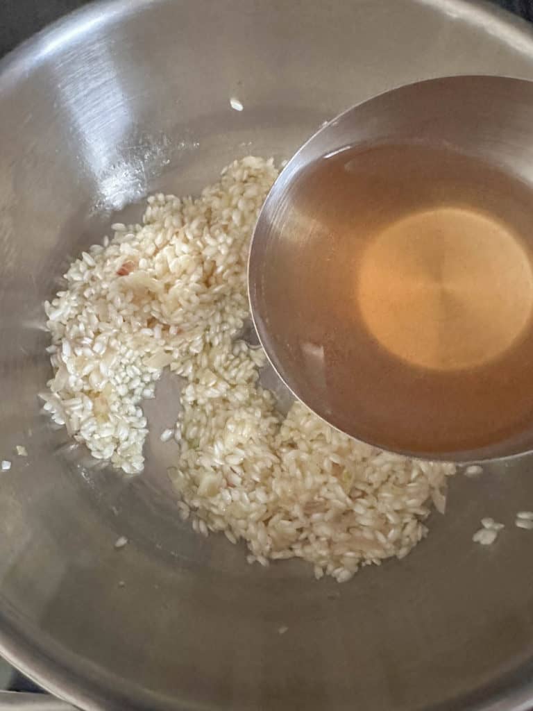 Adding broth to rice in pan for risotto.