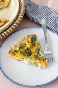 Slice of broccoli cheddar quiche on a white plate with blue rim.