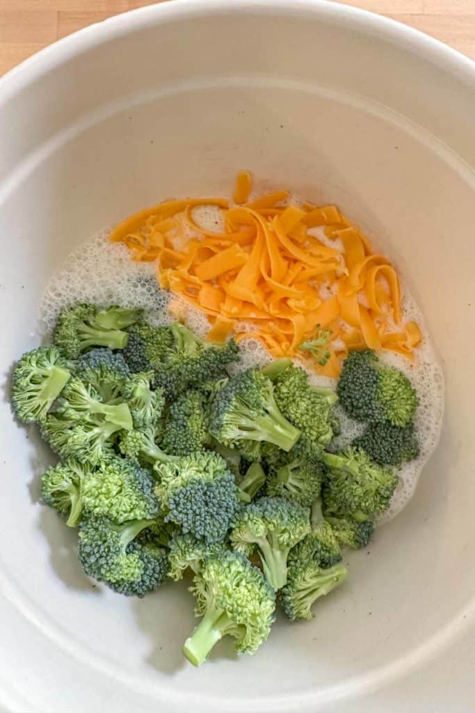 Broccoli and cheese added to quiche custard in mixing bowl.