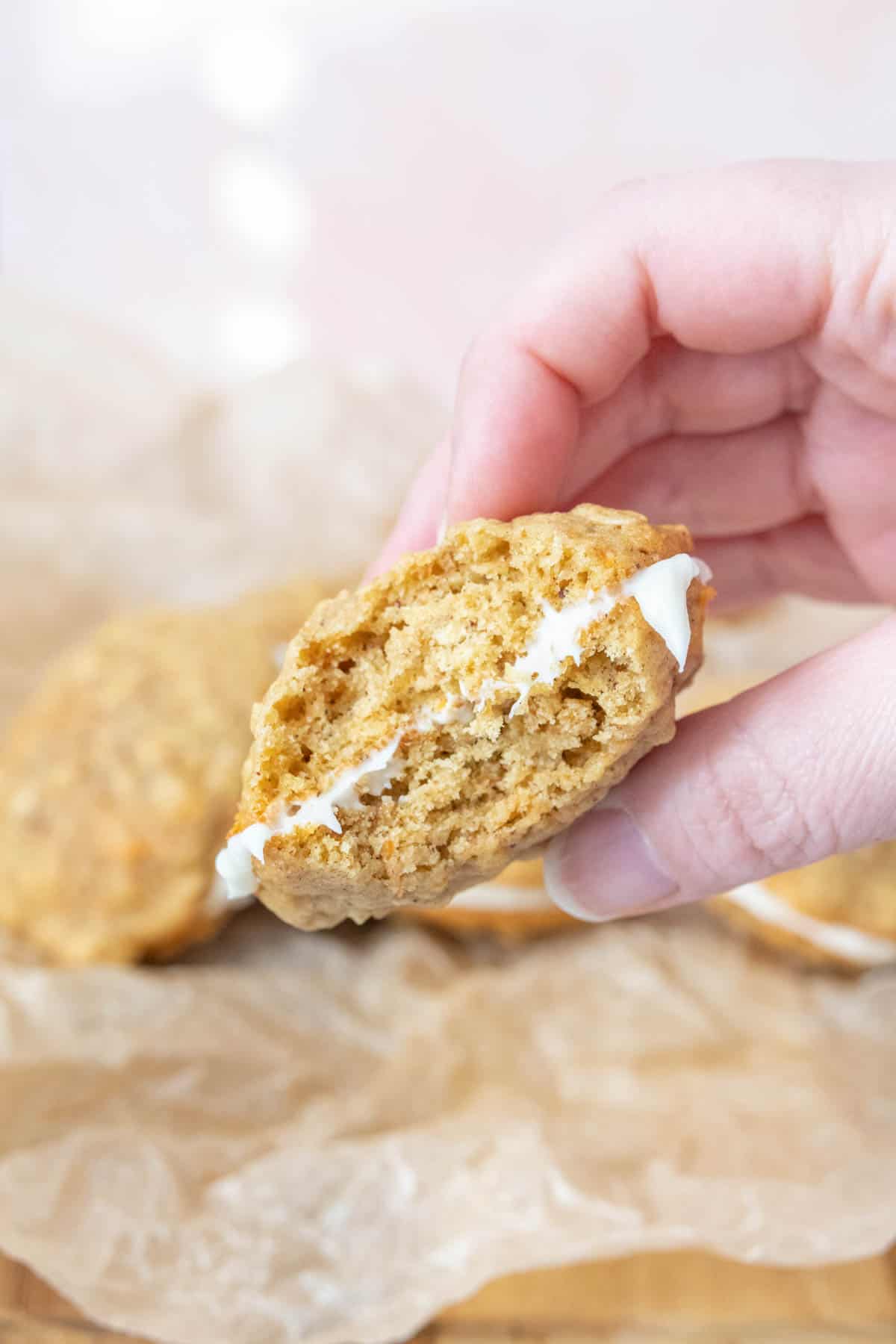 Caucasian hand holding carrot cake cookie with bite taken to show interior.