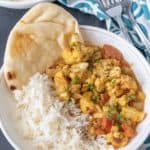 Cauliflower curry in a white bowl with rice and naan.