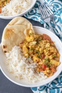 Cauliflower curry in a white bowl with rice and naan.