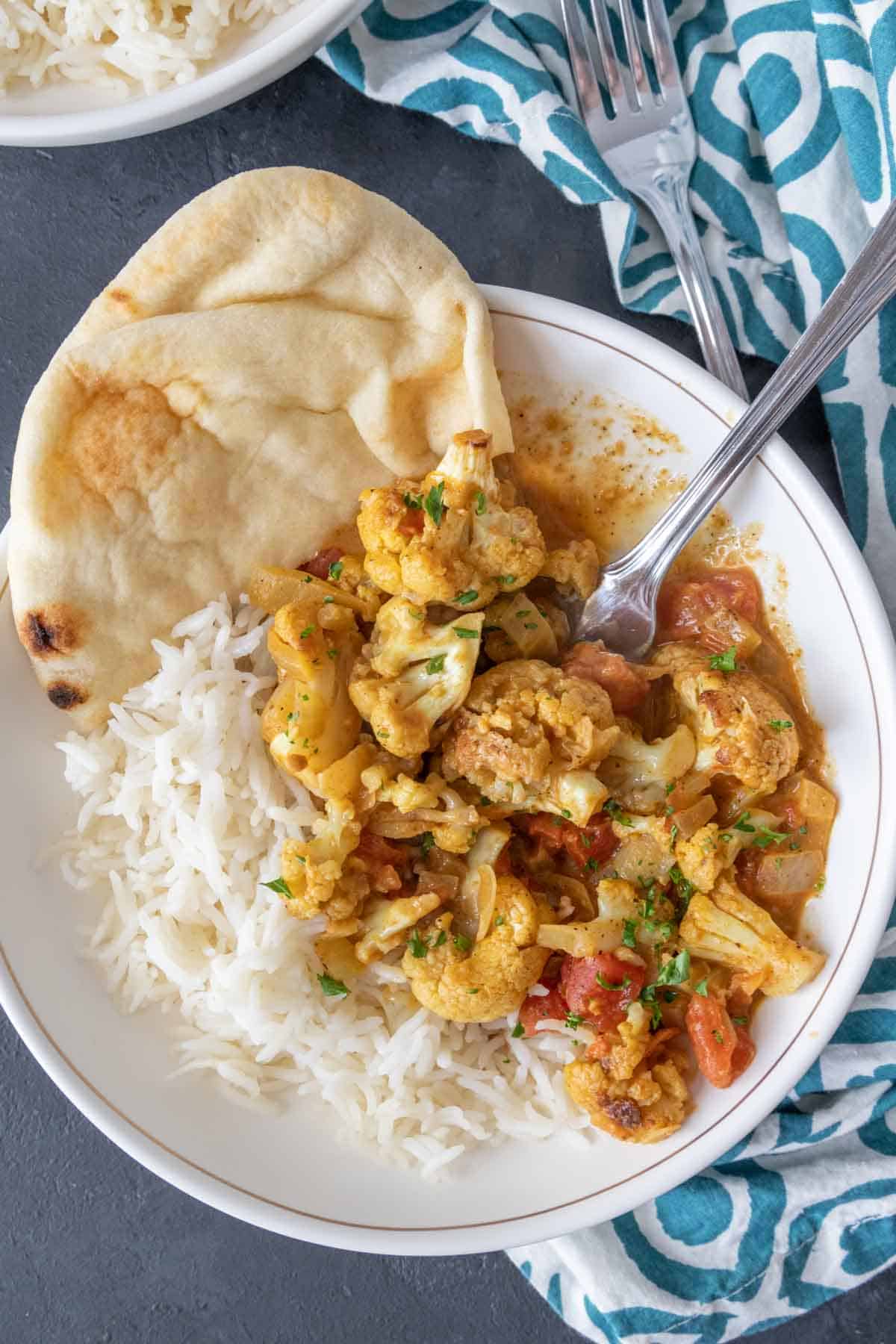 Overhead photo of cauliflower curry in a white bowl with rice and naan.
